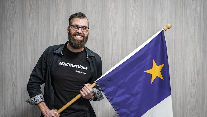 Mathieu Gingras, avec une barbe, tenant un drapeau acadien.