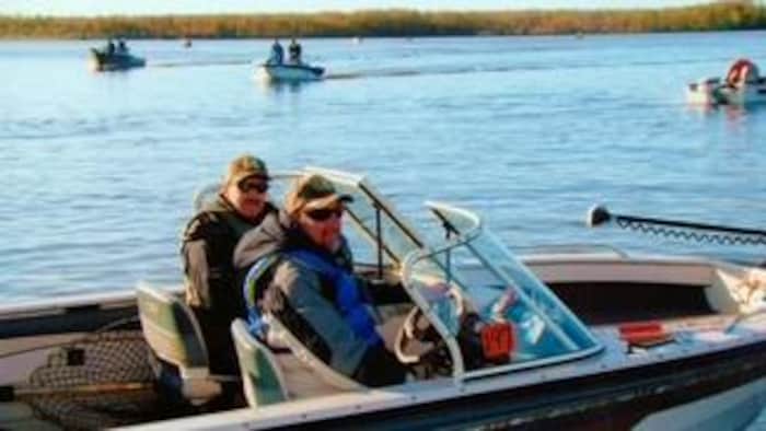 Deux hommes à bord d’un bateau de pêche — on voit quelques autres bateaux sur le lac en arrière-plan.