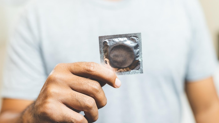 Un homme tient dans ses mains un préservatif.