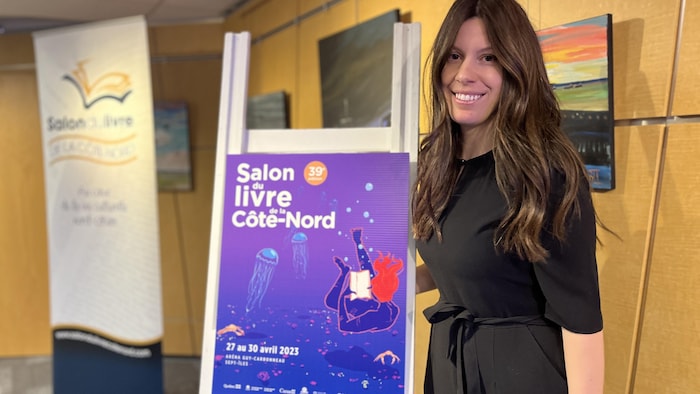 Mélanie Devost devant l'affiche de l'événement.