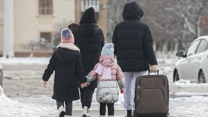 Une famille marche dans la rue en hiver avec une valise.