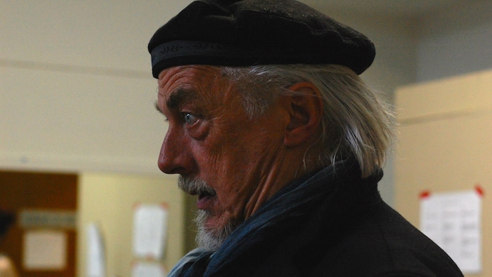 Michel Trépanier est de profil. Il porte un béret et un foulard.