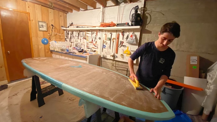 Une personne sable une planche à pagaie dans un atelier.