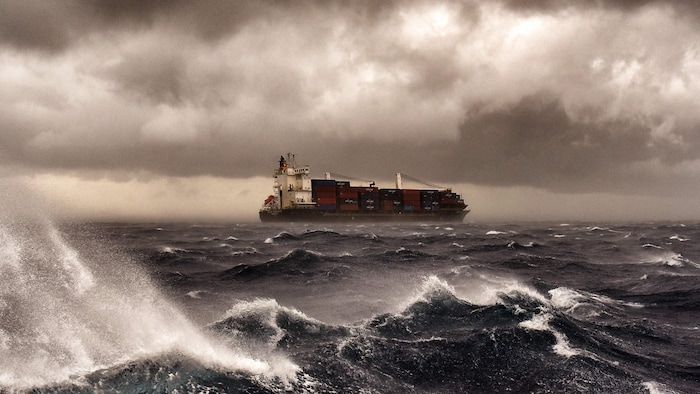 Un navire de charge navigue en pleine tempête sur une mer Méditerranée houleuse.