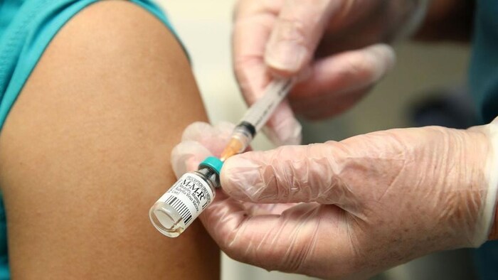 Un professionnel de la santé tient un flacon et une seringue alors qu'un patient est sur le point de se faire injecter un vaccin.