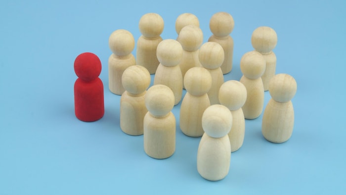 Des figurines beiges à côté d'une figurine rouge isolée des autres.