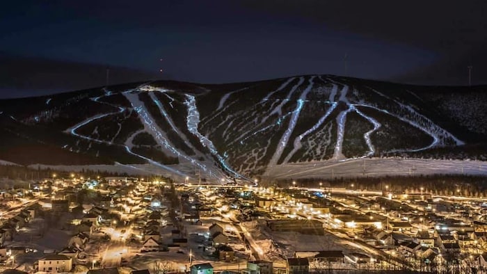 Un village éclairé au pied de montagne avec des pistes de skis lumineuses.