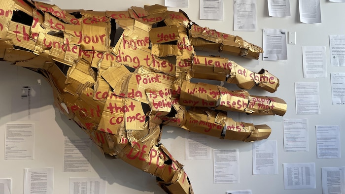 La main de la sculpture géante Limbo contre le mur au milieu des papiers d'immigration de l'artiste.
