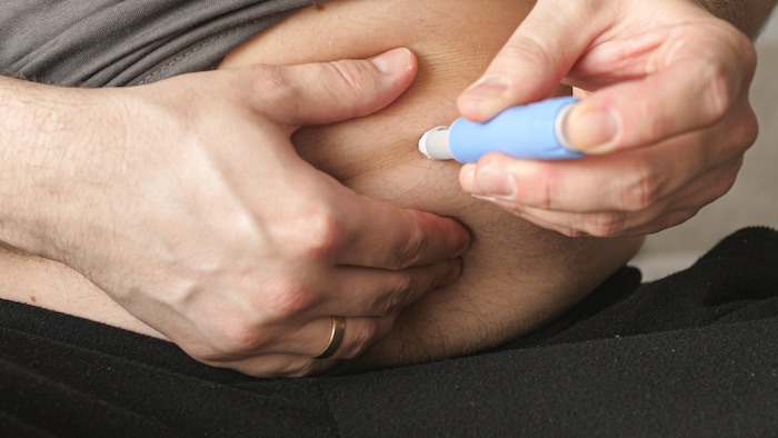 Gros plan sur le ventre d'un homme qui s'administre un médicament à l'aide d'un stylo injectable.  