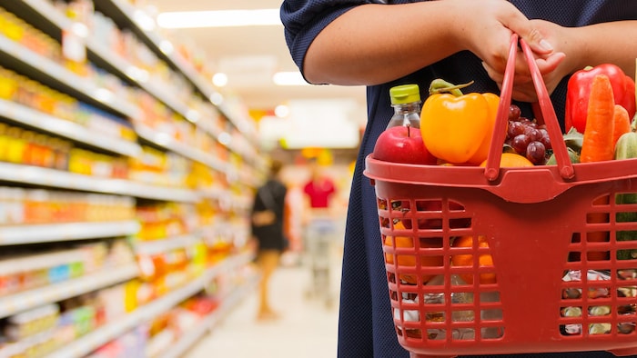 Une dame tient un panier de fruits et légumes dans une épicerie.