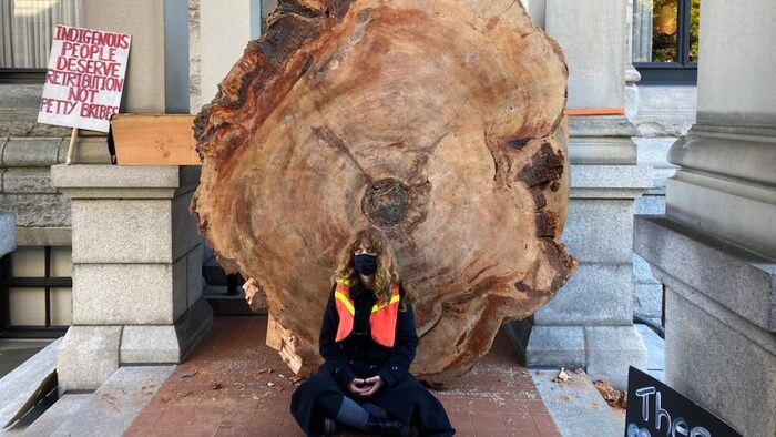 Une manifestante assise devant un immense tronc d'arbre.