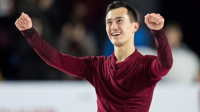 Patrick Chan sur la glace, les bras levés avec un grand sourire et un regard de satisfaction. 