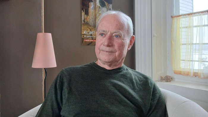 Paul Lachance est assis dans un fauteuil près d'une fenêtre. Il regarde vers la gauche.