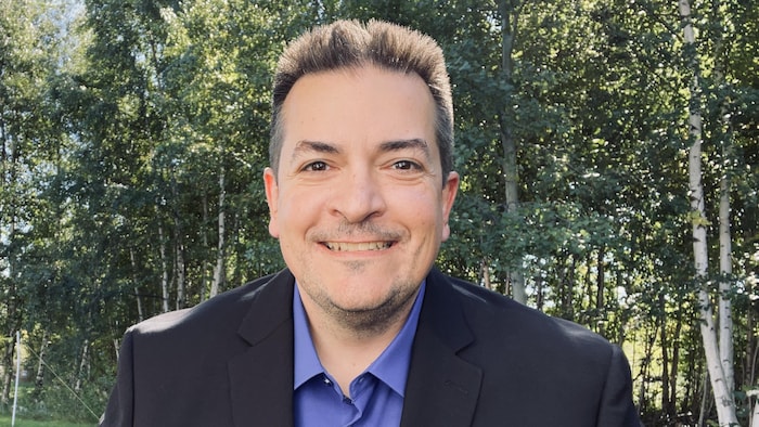 Paul Lavoie, directeur général de Développement économique Sept-Îles (DESI), souriant, dehors en été, avec des arbres feuillus derrière lui.