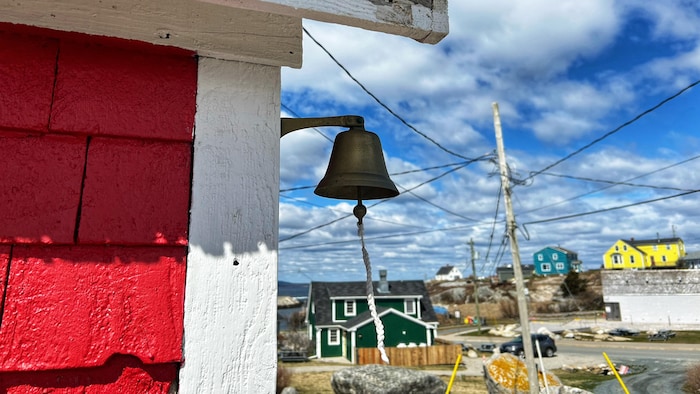Une cloche d'école à l'extérieur avec en arrière-plan le village de Peggy's Cove.