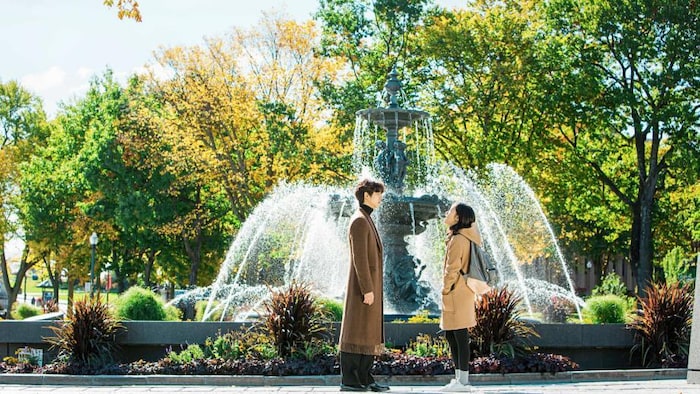 Un homme et une femme discutent face à face devant une fontaine.