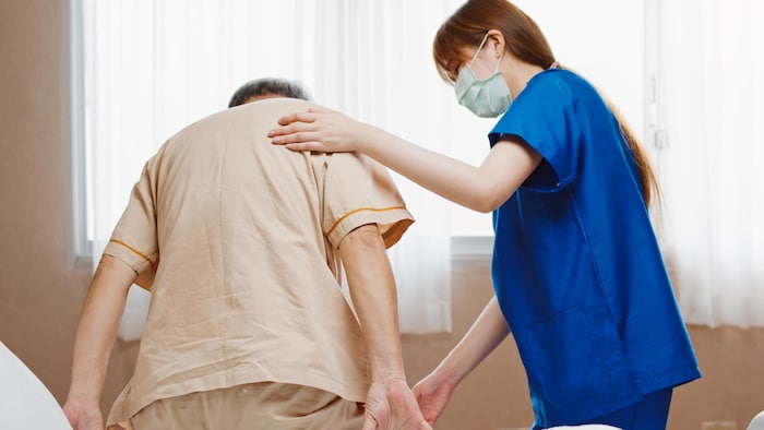 ممرّضة تساعد رجلا مسنّا على النهوض من سريره.