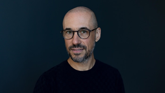 Jean-Philippe Pleau, sur fond noir, sourit au photographe.
