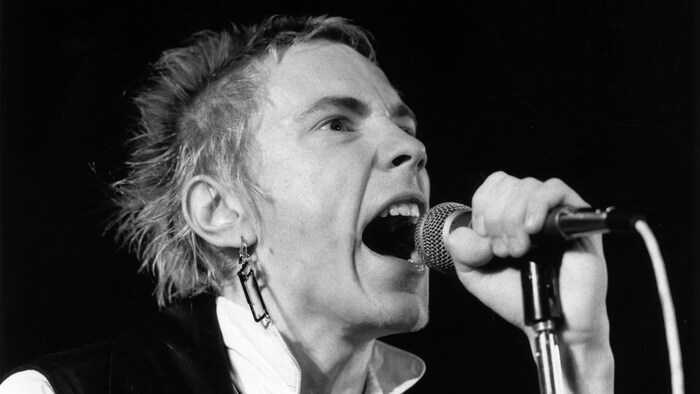  Johnny Rotten en train de chanter, un micro dans la main. 