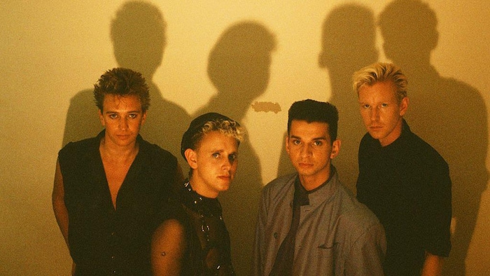 Photo dans un studio où l'on voit les quatre membres du groupe et leurs ombres projetées au mur.