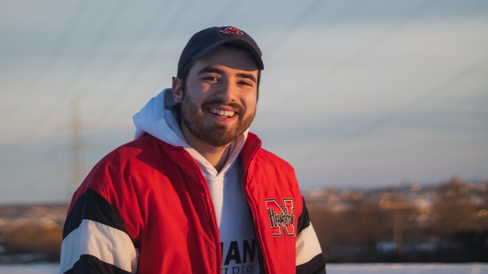 Jérémy Lévesque sourit devant un paysage enneigé, le manteau ouvert et une casquette sur la tête.