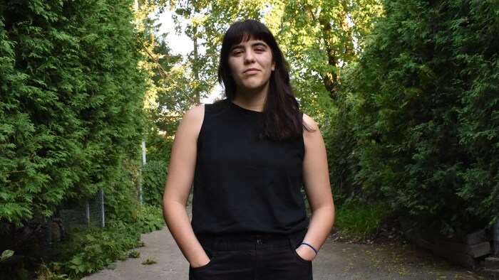 L'autrice est debout au milieu dans un sentier, en nature, les mains dans les poches de son pantalon.