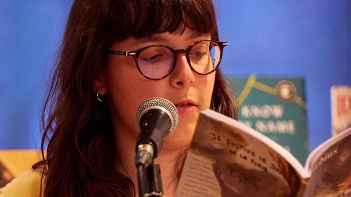 L'autrice est derrière un micro, en train de lire un ouvrage.