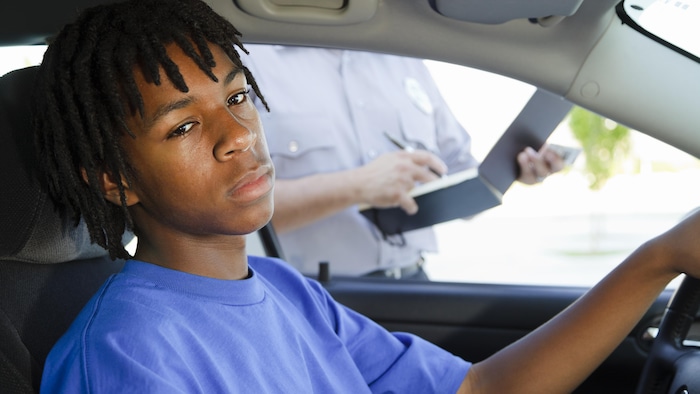 Un jeune homme noir au volant d'une voiture se fait contrôle par un policier. 