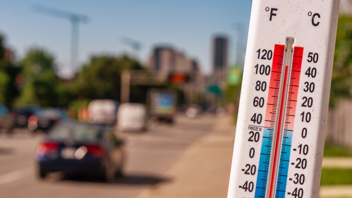 Un thermomètre devant des voitures pendant une canicule à Montréal.