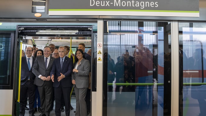 La mairesse de Montréal, Soraya Martinez Ferrada, à droite, à côté des premiers ministres Mark Carney et François Legault, ainsi que le PDG de La Caisse, Charles Emond, à gauche, à bord d'une voiture du REM lors de l'inauguration de l'antenne Deux-Montagnes, le vendredi 14 novembre 2025.