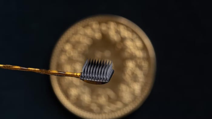 Une pastille carrée connectée à un fil contient 64 microélectrodes en forme d'aiguilles.  
