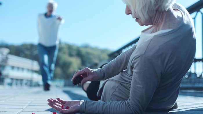 Une dame tombe et perd ses médicaments tandis qu'un homme accourt vers elle.