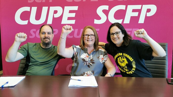 Trois dirigeants du SCFP brandissent le poing.