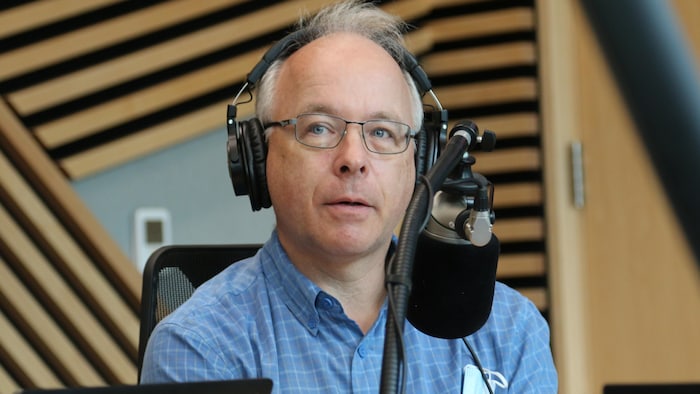 Un homme, casque d'écoute sur la tête, regarde attentivement dans la direction de l'animateur alors qu'il est assis dans un studio de radio. 
