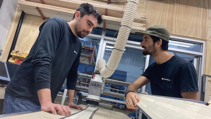 Deux hommes discutent autour de planches de skis dans un atelier.