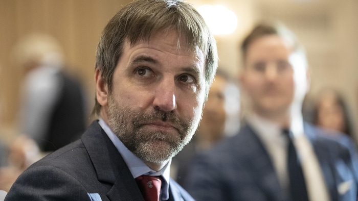 Le ministre Guilbeault assis dans une salle, entouré d'autres personnes.