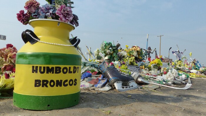 Un pot de fleurs vert et jaune sur lequel il est inscrit Humbolt Broncos, accompagné de plusieurs objets significatifs, comme des patins à glace. 