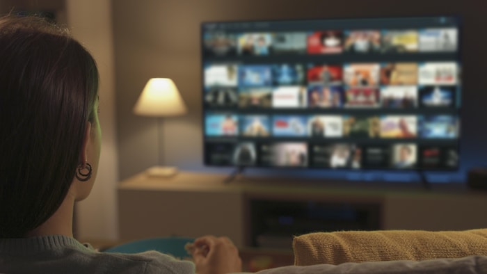 Une femme assise dans son salon regarde la télévision montrant une sélection de contenus sur une plateforme de diffusion en continu.