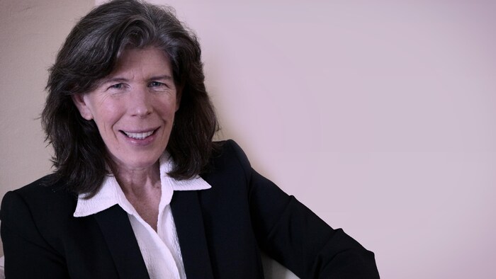 Susan O'Donnell, blouse blanche sur veste noire, photographiée devant un mur pâle.