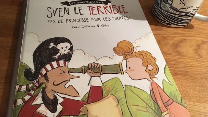 On voit la couverture d'un livre jeunesse. Un pirate regarde la figure d'une jeune fille à travers une longue-vue.