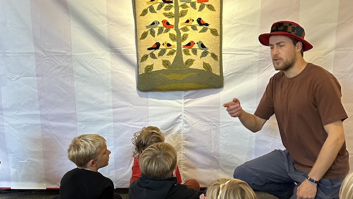 Un animateur présente un tapis hooké à un groupe d'enfants.