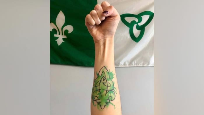 Tatouage d'un drapeau franco-ontarien sur l'avant bras, devant un drapeau franco-ontarien.
