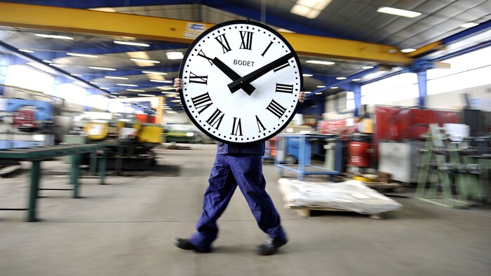 Un employé d'une compagnie française d'horloges transporte une horloge.