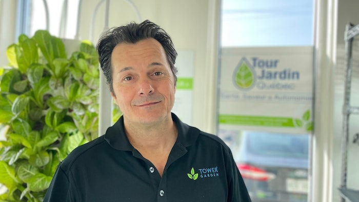 Un homme sourit à la caméra, on voit des plantes derrière lui.