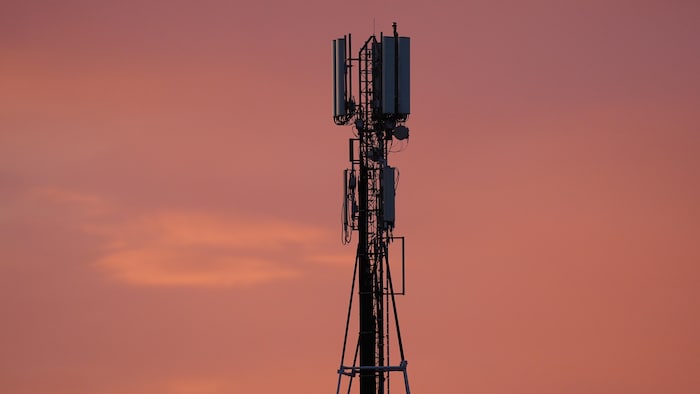 Une tour de télécommunication se découpe en contre-jour sur un ciel de coucher de soleil. 