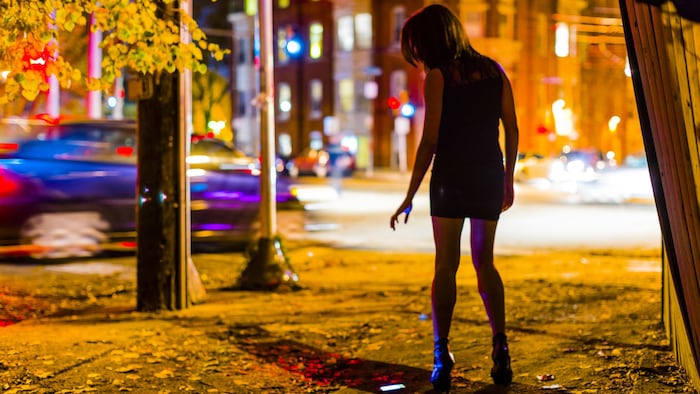 Une jeune femme seule au coin d'une rue d'une grande ville la nuit, avec un téléphone portable tombé au sol.