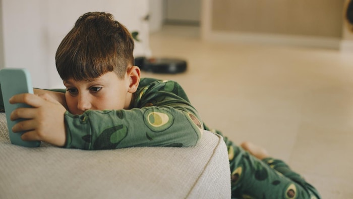 Un jeune garçon regarde son cellulaire en pyjama.