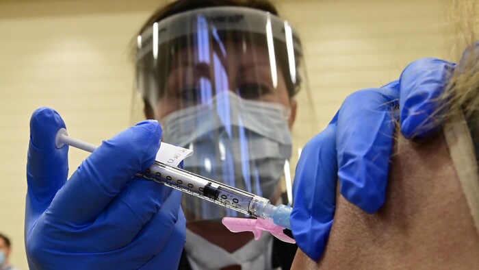 Une femme masquée administre un vaccin.