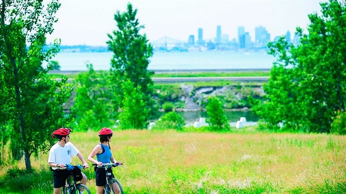 Deux cyclistes au parc national des Îles-de-Boucherville. On aperçoit la ville de Montréal et le pont Jacques-Cartier au loin.
