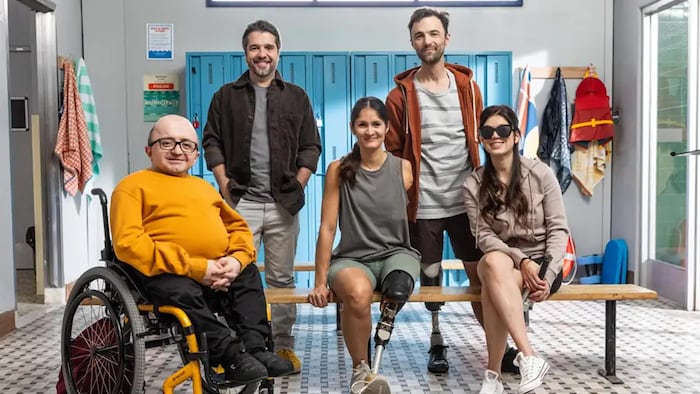 Dans un vestiaire, Michel Cordey est assis sur une un fauteuil roulant, Camille Chai et Jacques Poulin-Denis portent une prothèse tibiale, et Marie-Christine Ricignuolo porte des verres fumés. 
